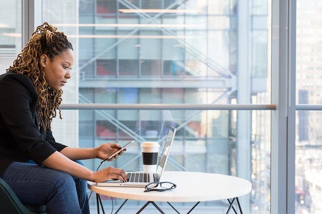 Woman working at coffee shop on phone and laptop